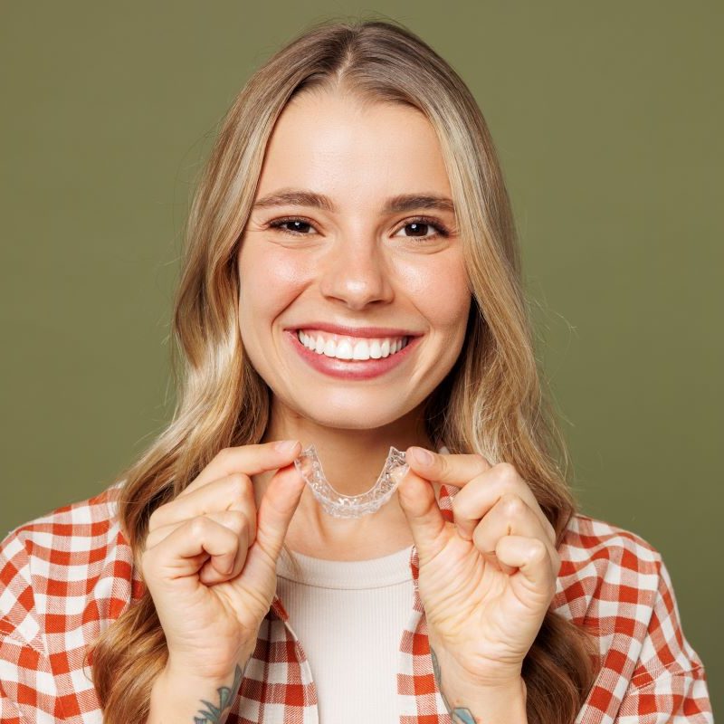 Blonde woman holding Invisalign aligner, smiling in Sandy, Oregon.