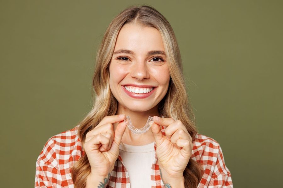 Blonde woman holding Invisalign aligner, smiling in Sandy, Oregon.