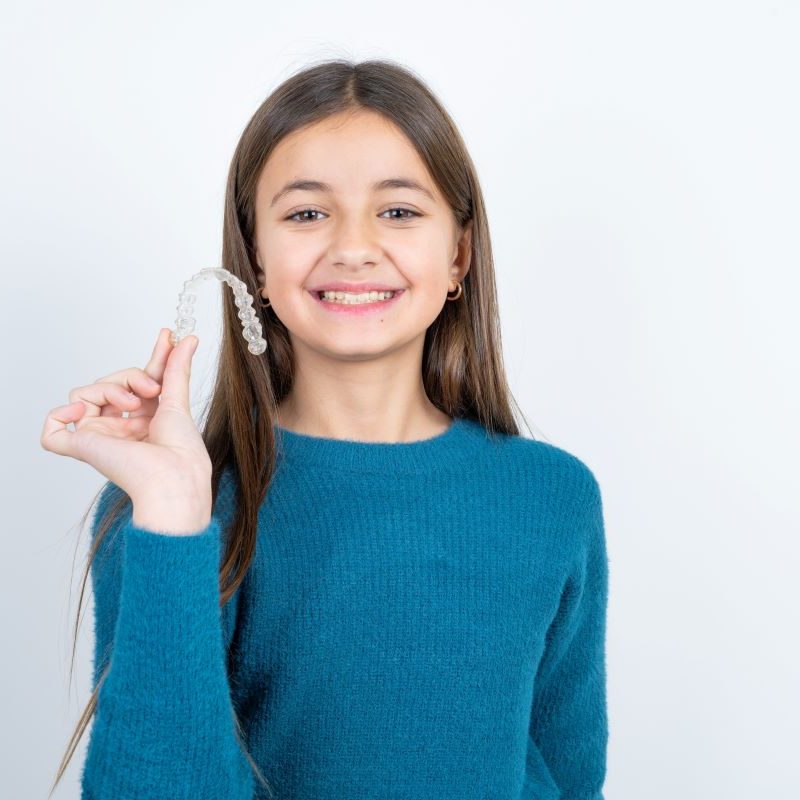 Girl smiling holding clear dental aligners in Sandy, Oregon