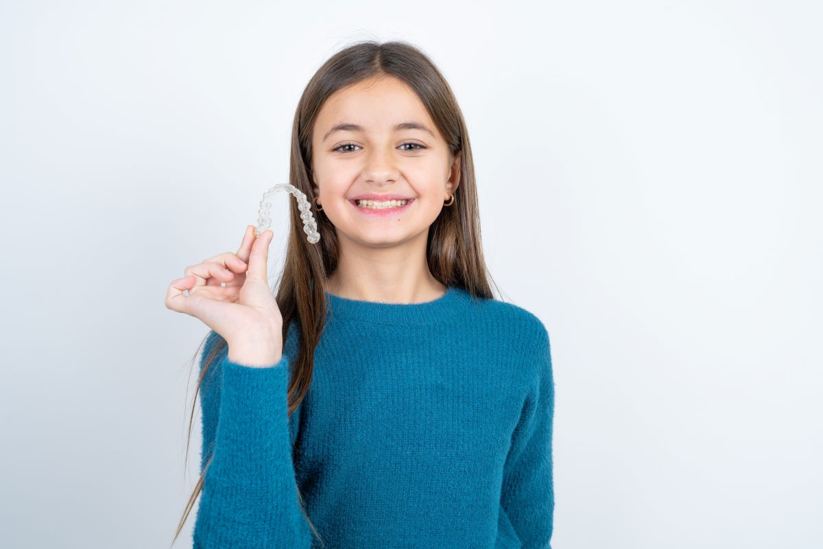 Girl smiling holding clear dental aligners in Sandy, Oregon